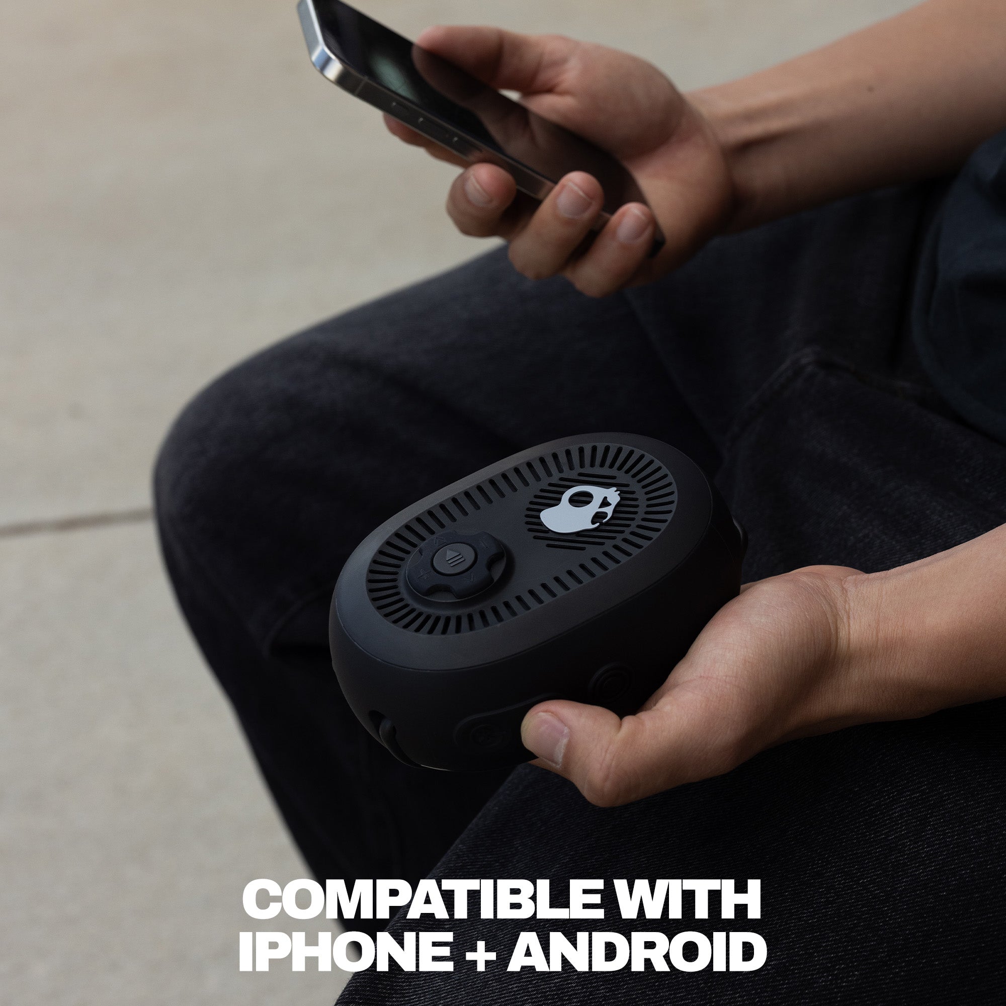 Person holding a device with a smartphone, text 'Compatible with iPhone + Android' on a neutral background | True Black
