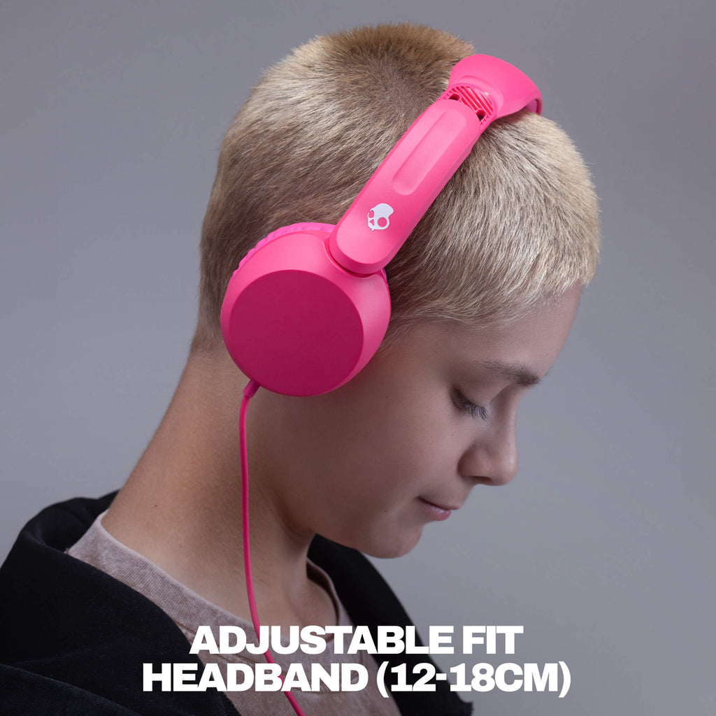 A person with short blonde hair wearing bright pink over-ear headphones with a visible pink cable, shown against a gray studio background with the text 'ADJUSTABLE FIT HEADBAND (12-18CM)' at the bottom. | Crazy Pink