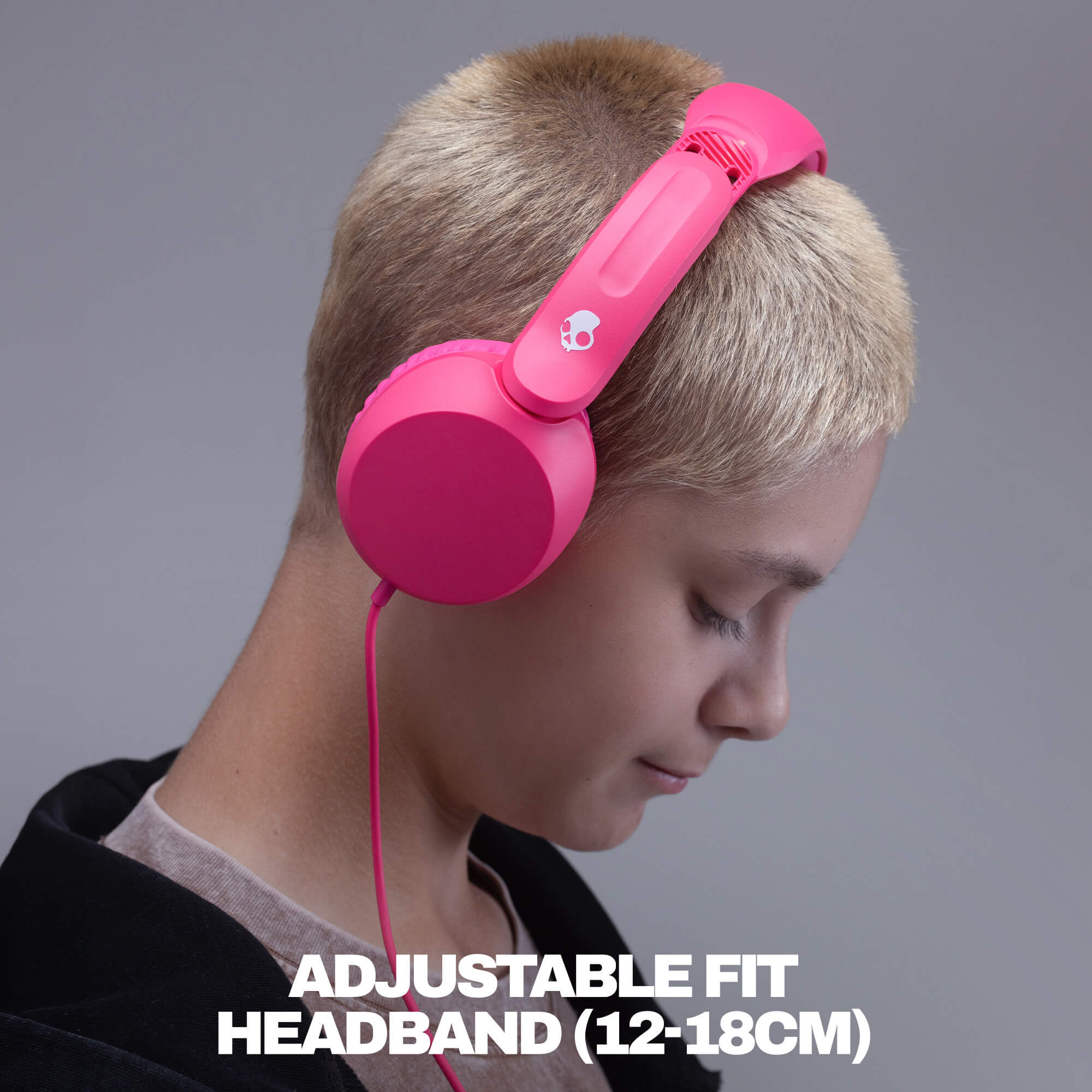 A person with short blonde hair wearing bright pink over-ear headphones with a visible pink cable, shown against a gray studio background with the text 'ADJUSTABLE FIT HEADBAND (12-18CM)' at the bottom. | Crazy Pink