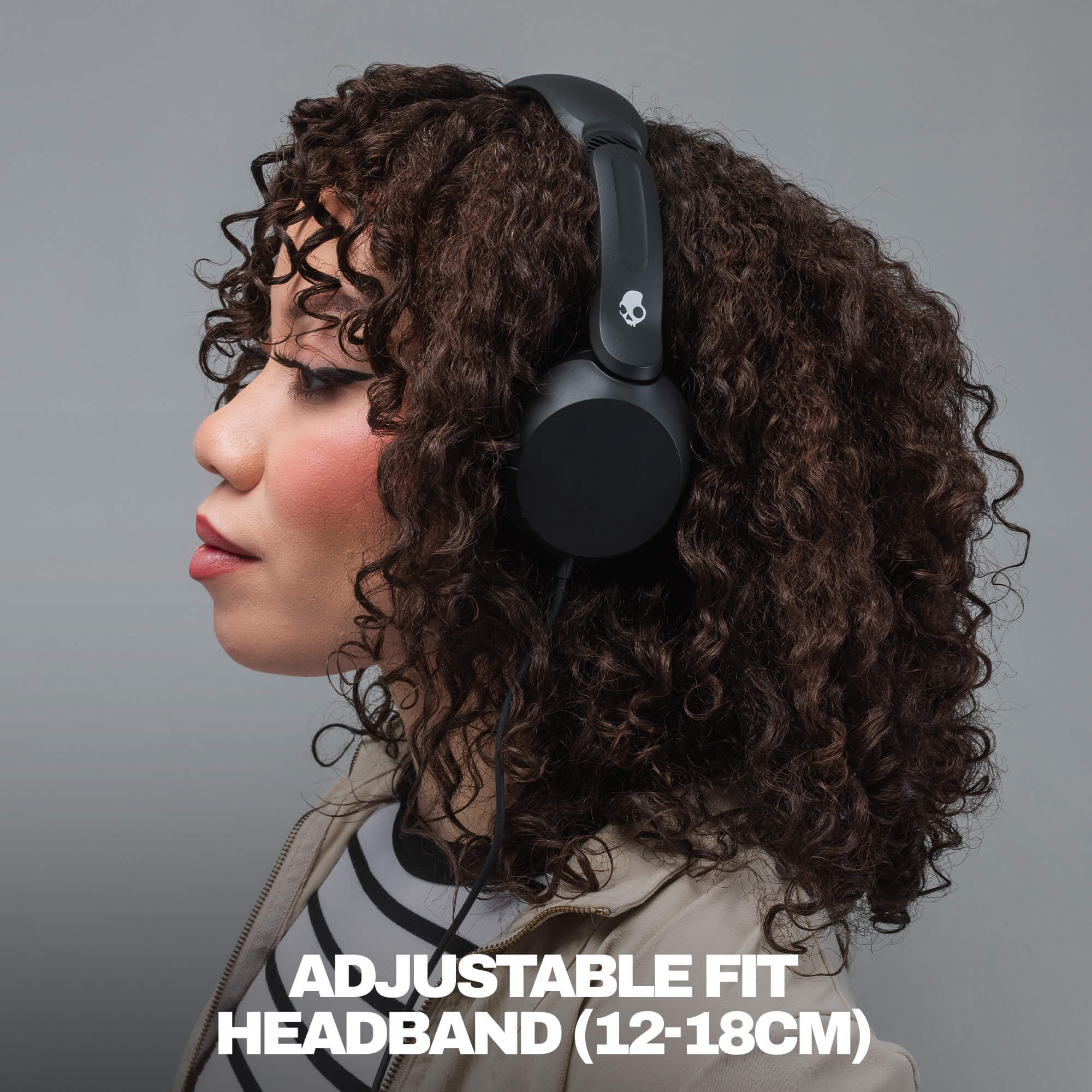 A woman in profile wearing black over-ear headphones with curly brown hair, against a plain gray studio background. White text at the bottom reads 'ADJUSTABLE FIT HEADBAND (12-18CM)'. | True Black