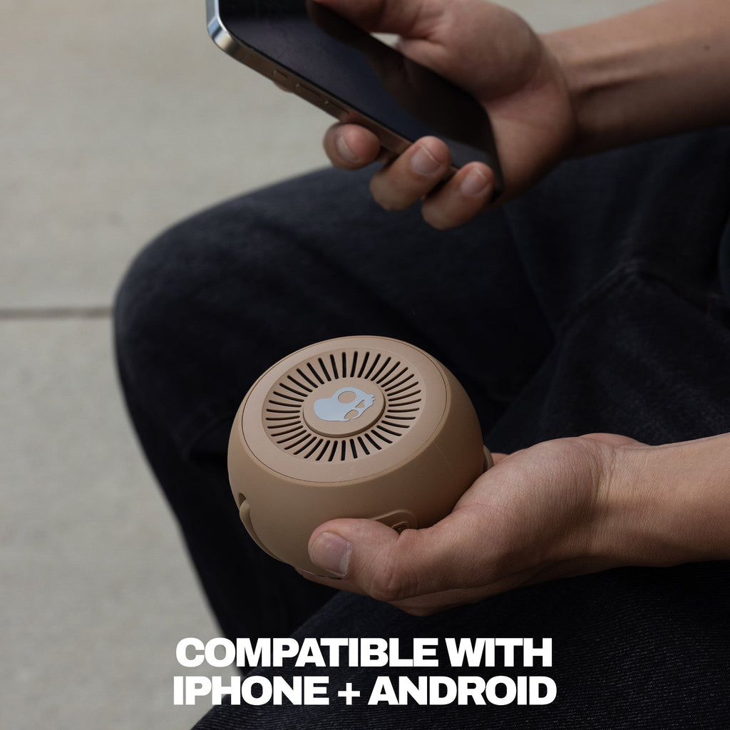 Person holding a smartphone and a small brown speaker, with text indicating compatibility with iPhone and Android. | Primer