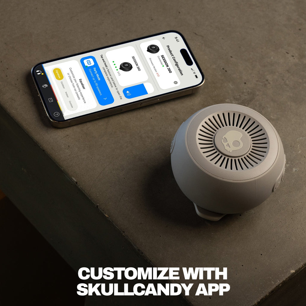Smartphone displaying an app interface next to a cylindrical device on a concrete surface with text 'Customize with Skullcandy App'. | Cement