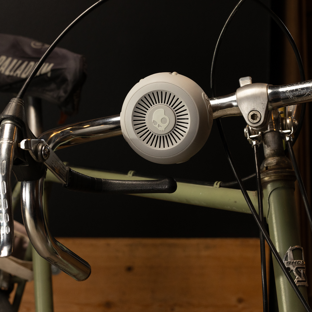 Bicycle handlebar with a white speaker attached against a dark background | Cement