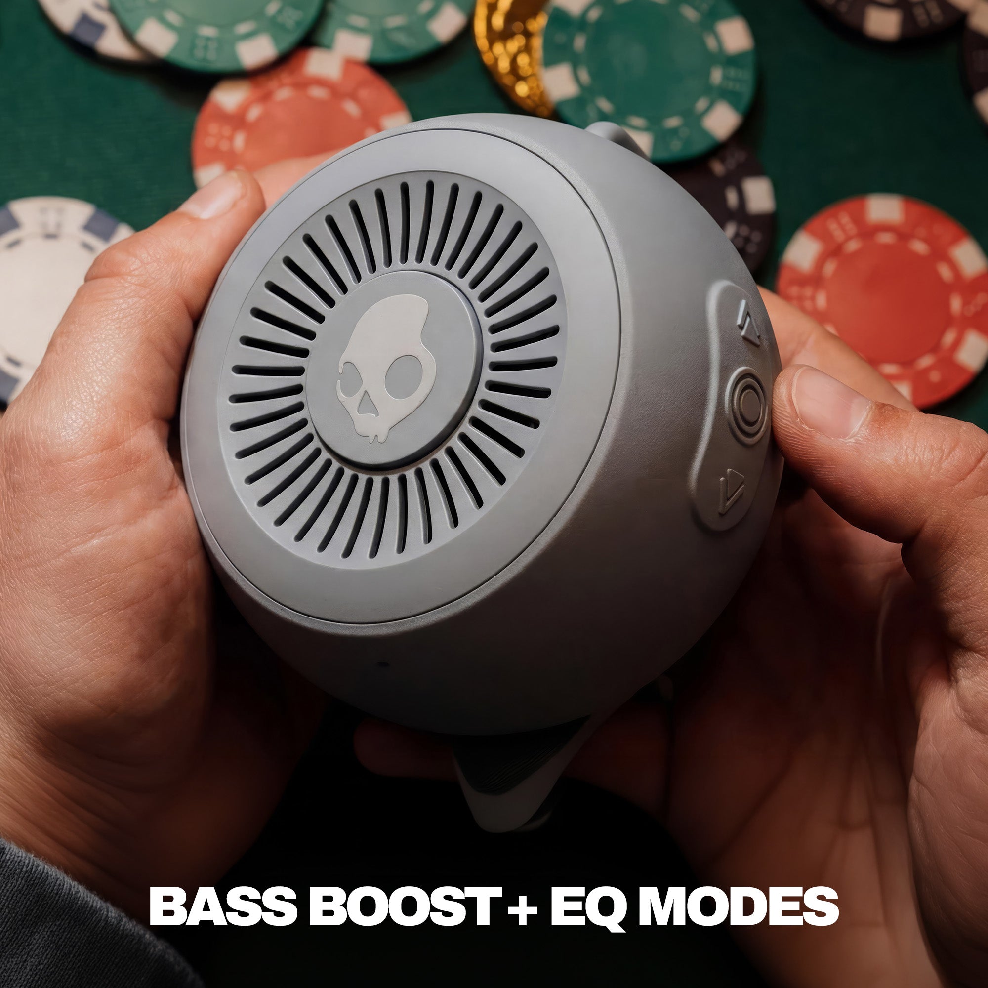 Gray speaker with control buttons held by hands against a poker chip background | Cement