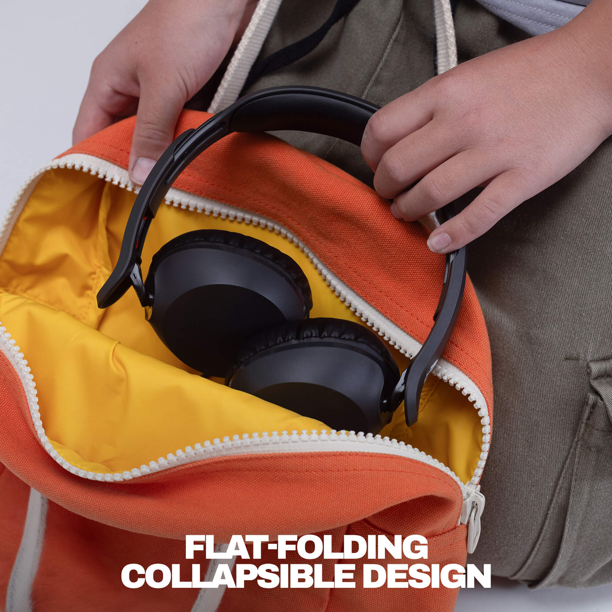 A close-up of a person's hands placing black over-ear headphones inside an orange and yellow zippered bag, with the text 'FLAT-FOLDING COLLAPSIBLE DESIGN' at the bottom. | True Black