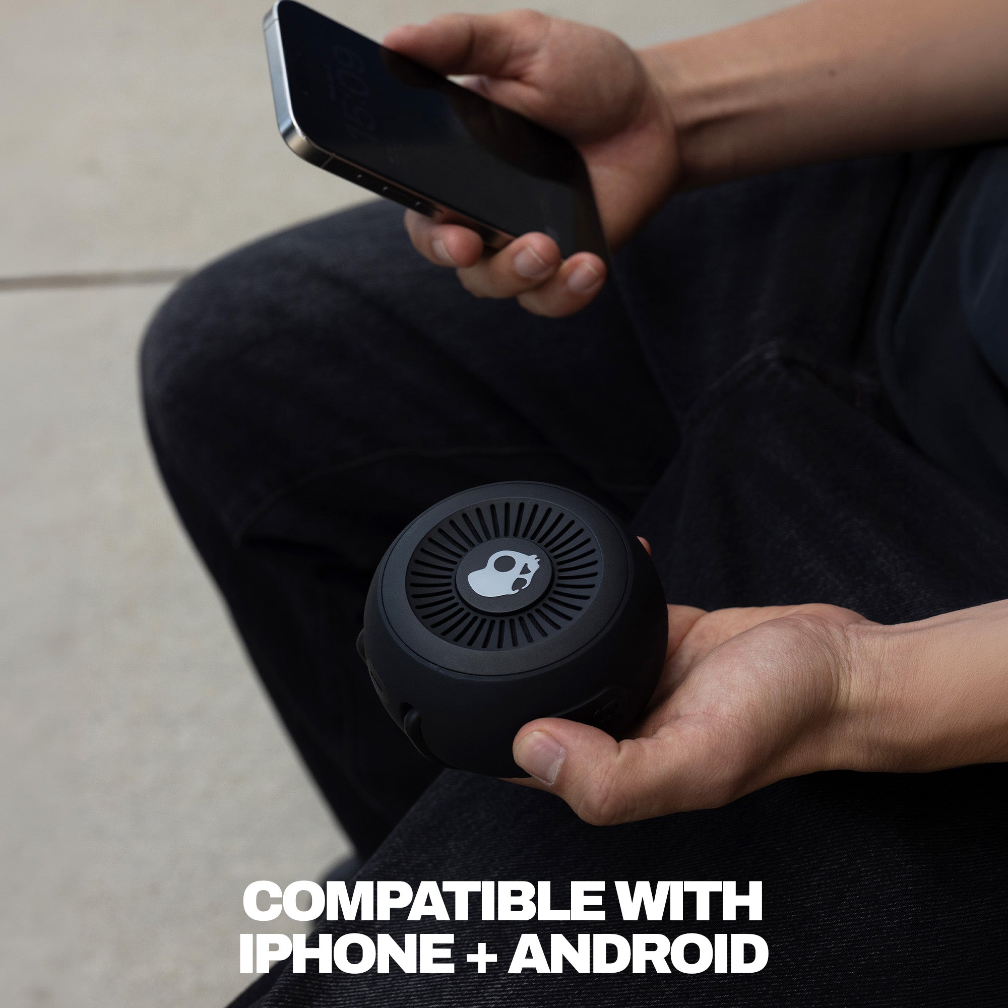 Person holding a black portable speaker and smartphone with text 'Compatible with iPhone + Android'. | True Black